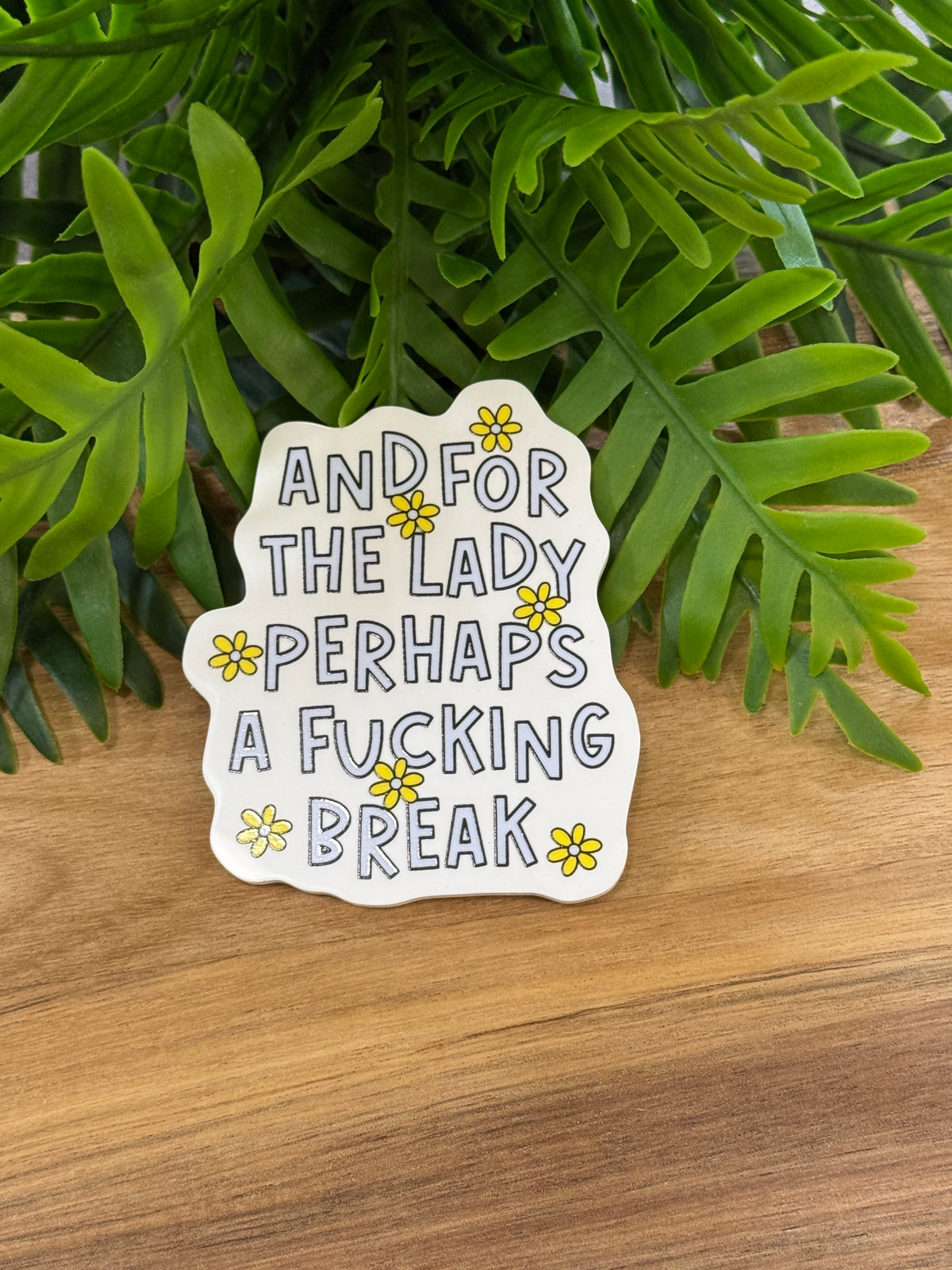 White acrylic magnet with yellow daisies and the phrase And for the lady perhaps a fucking break