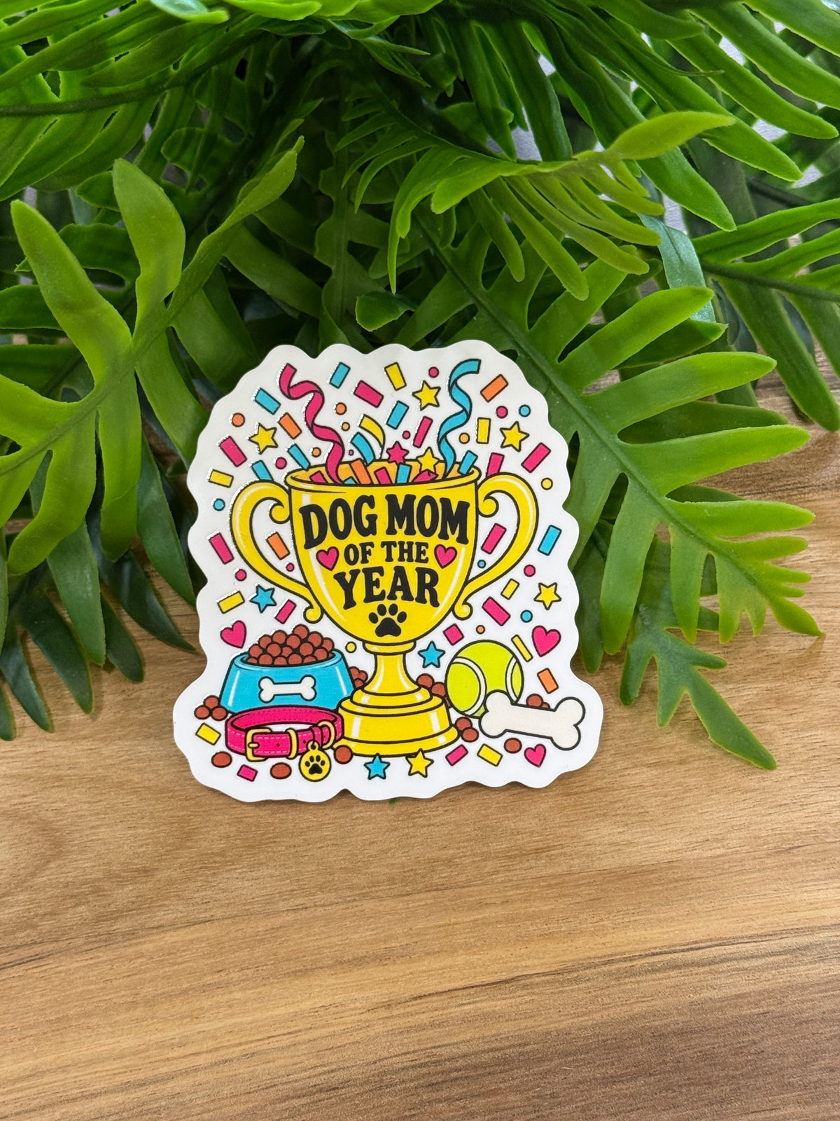 Dog Mom of the Year acrylic magnet featuring a yellow trophy, colorful confetti, dog bowl, collar, tennis ball, and bone