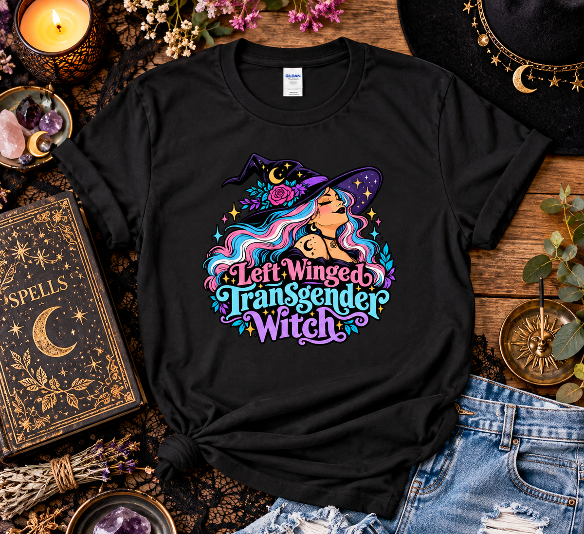 Black t-shirt with a Left Winged Transgender Witch design featuring a witch with pink and blue hair, roses, moons, and stars