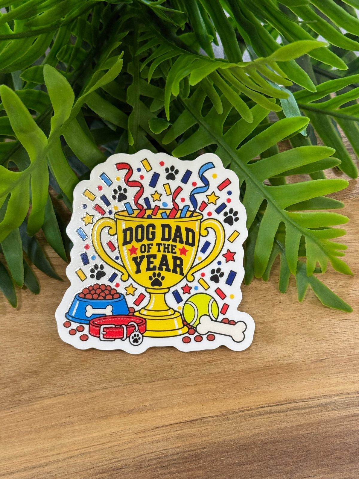 Dog Dad of the Year acrylic magnet with a yellow trophy, paw prints, confetti, blue dog bowl, red collar, tennis ball, and bone