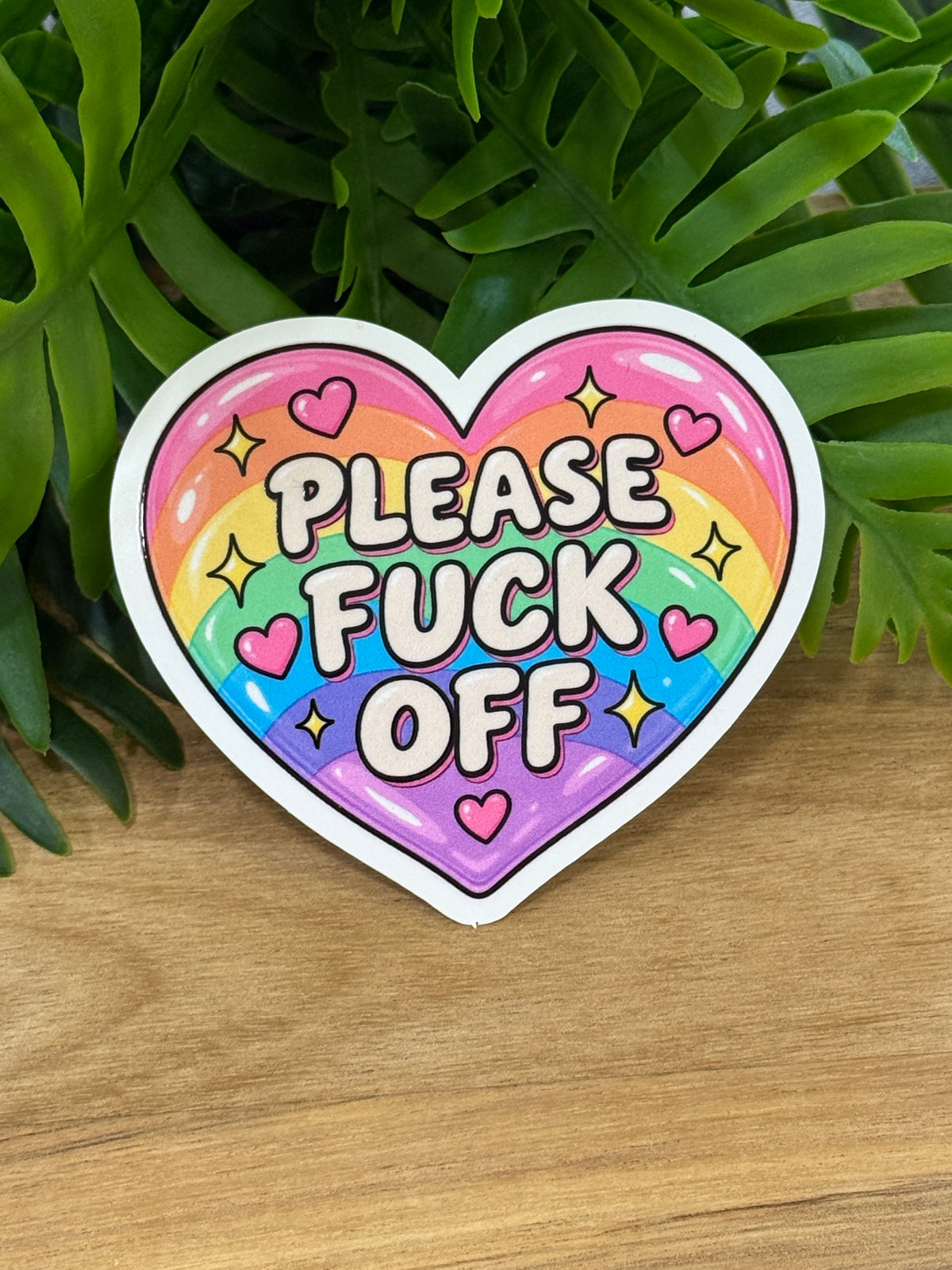 Pastel rainbow heart vinyl sticker reading Please Fuck Off with pink hearts, yellow sparkles, and a white border